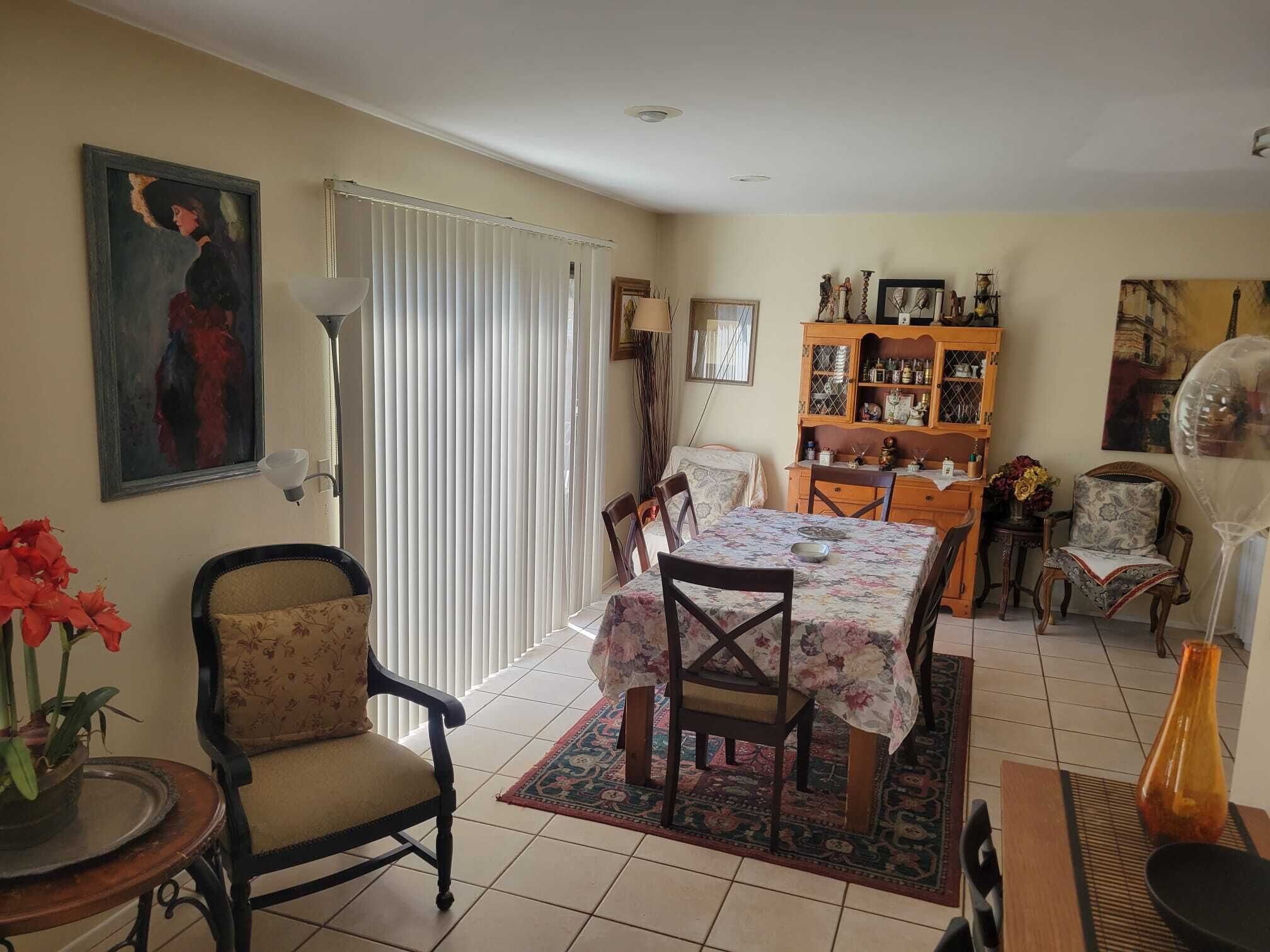 Un coin repas avec une table dressée pour quatre personnes, entourée de chaises, un buffet en bois avec des portes en verre et un tableau accroché au mur.