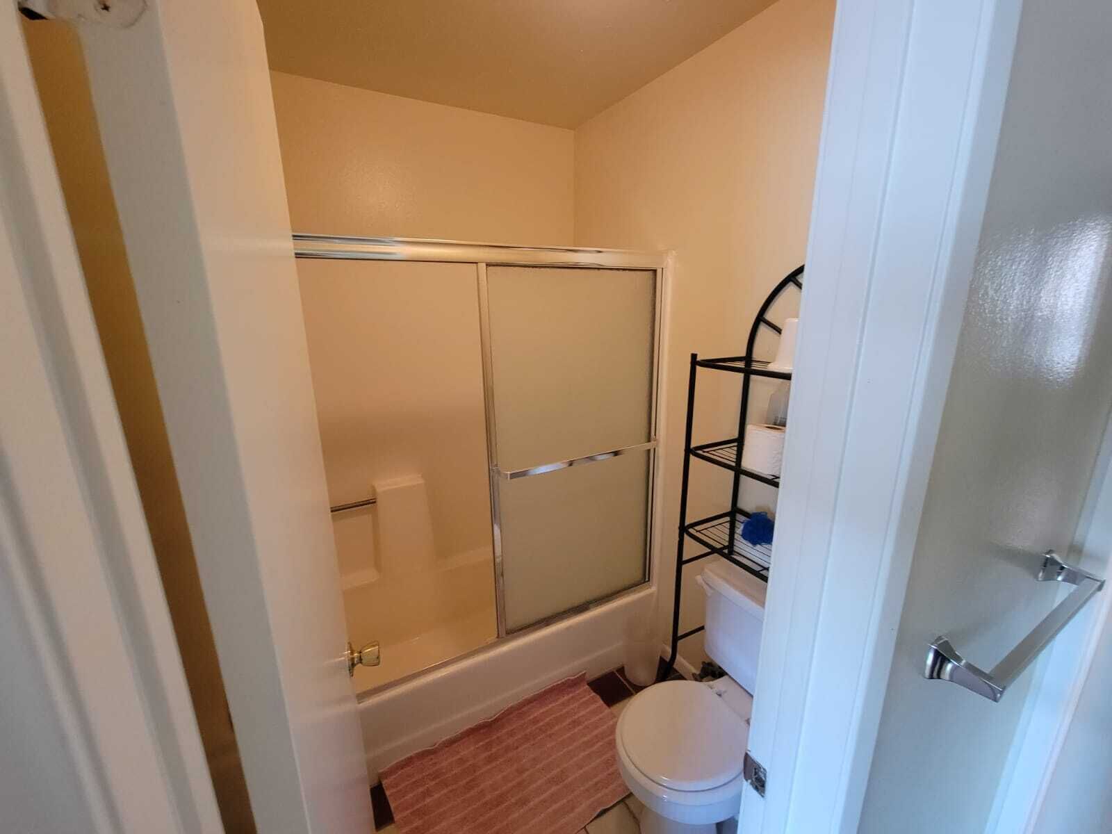 Un baño con ducha, inodoro y un estante con artículos de aseo.