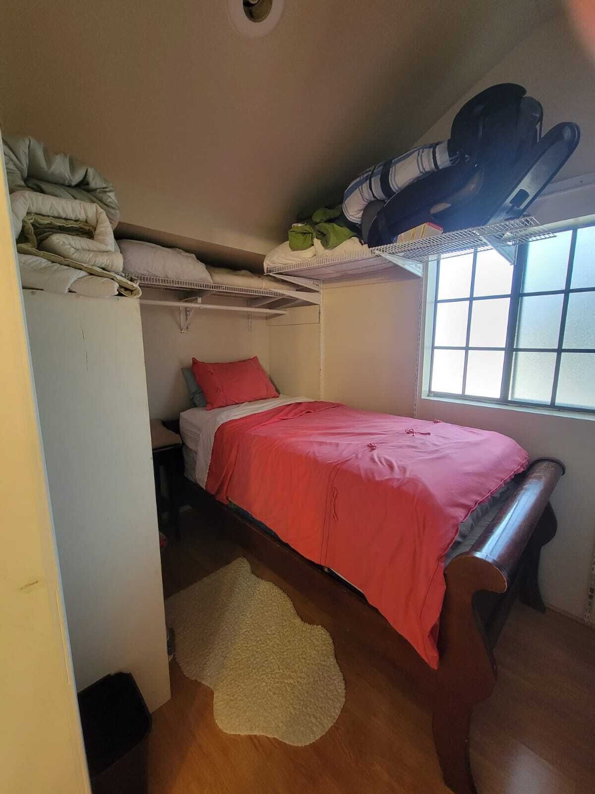 Ein kleines, kompaktes Schlafzimmer mit einem Einzelbett, einem Fenster mit Jalousien und einem Hochschlafplatz darüber.