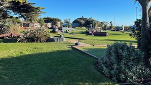 Un parque bien cuidado con diversos árboles, una gran escultura esférica y un edificio distante con una cúpula.