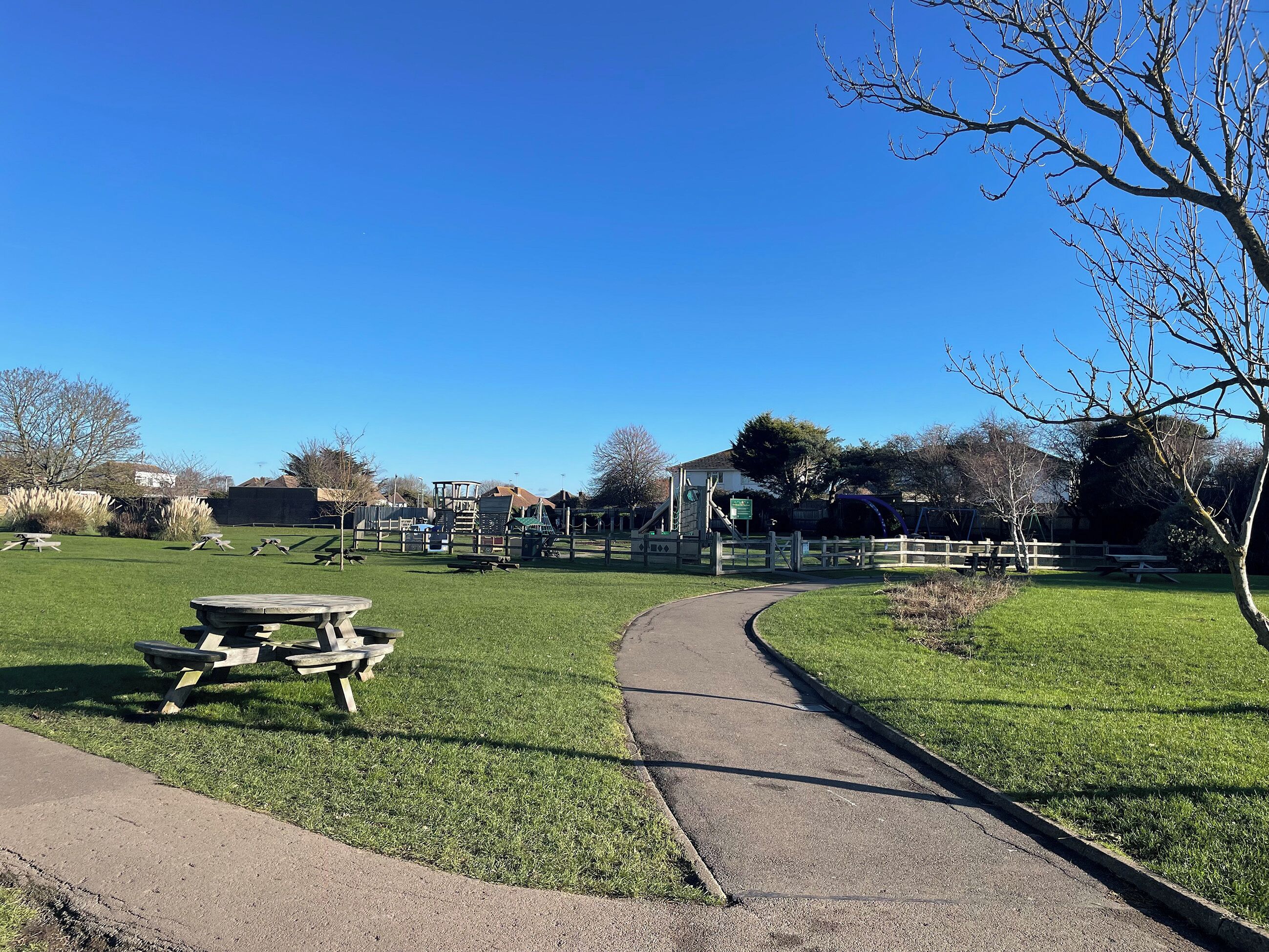 A park with a picnic table, playground equipment, and a pathway.