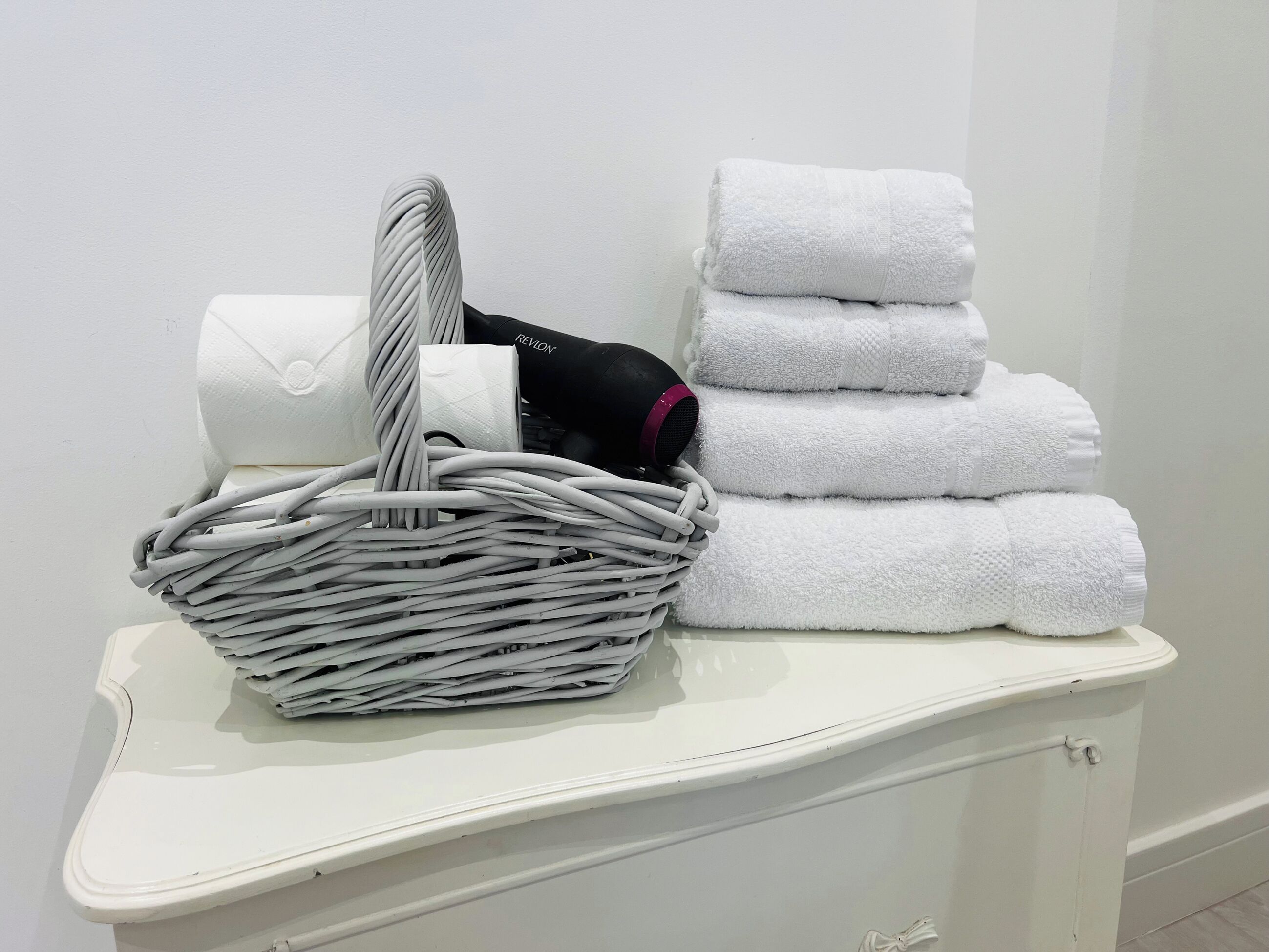 A white bathroom vanity with a wicker basket containing a white towel, a black hairdryer, and a white towel.