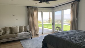 Un dormitorio con cama, sofá y vistas a un campo de golf a través de amplias ventanas.