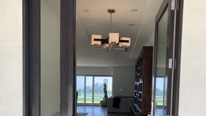 Un interior moderno con suelo de madera, un amplio ventanal corredera que da a un balcón y una lámpara en el techo.