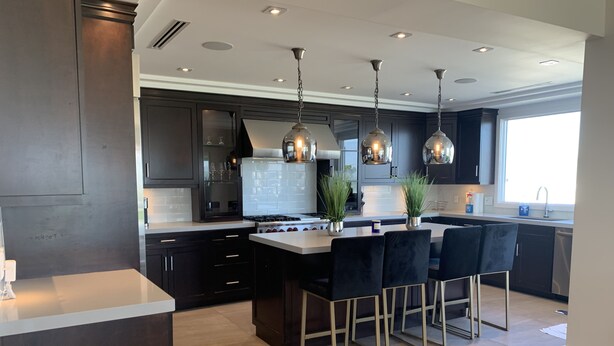Una cocina moderna con muebles oscuros, una isla central con taburetes altos, iluminación colgante y un amplio ventanal que proporciona luz natural.
