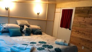 Ein Schlafzimmer mit einem Bett, Kissen, einem roten Vorhang und einer Holzwand.