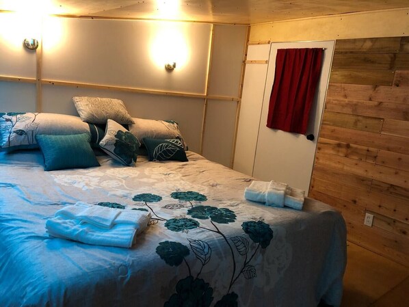 Un dormitorio con cama, almohadas, una cortina roja y una pared de madera.
