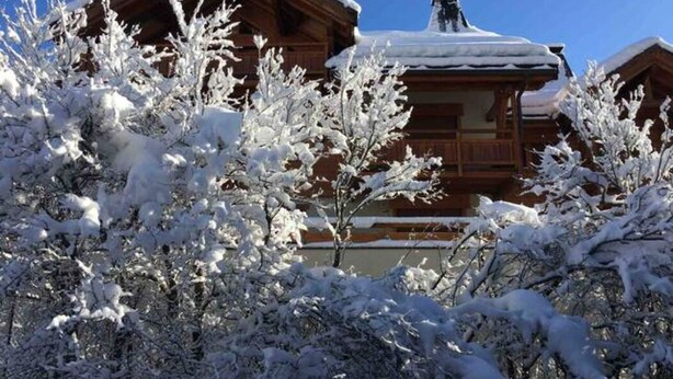 Una cabaña de madera con techo cubierto de nieve, rodeada de árboles cargados de nieve.