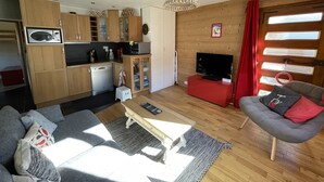 Un espacio habitable compacto con kitchenette, comedor, sofá, televisor y ventana con cortinas.