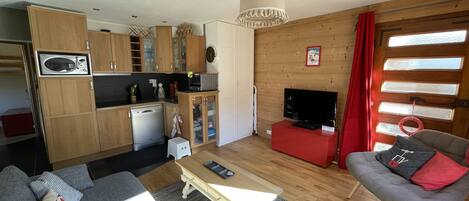 Un espacio habitable compacto con kitchenette, comedor, sofá, televisor y ventana con cortinas.