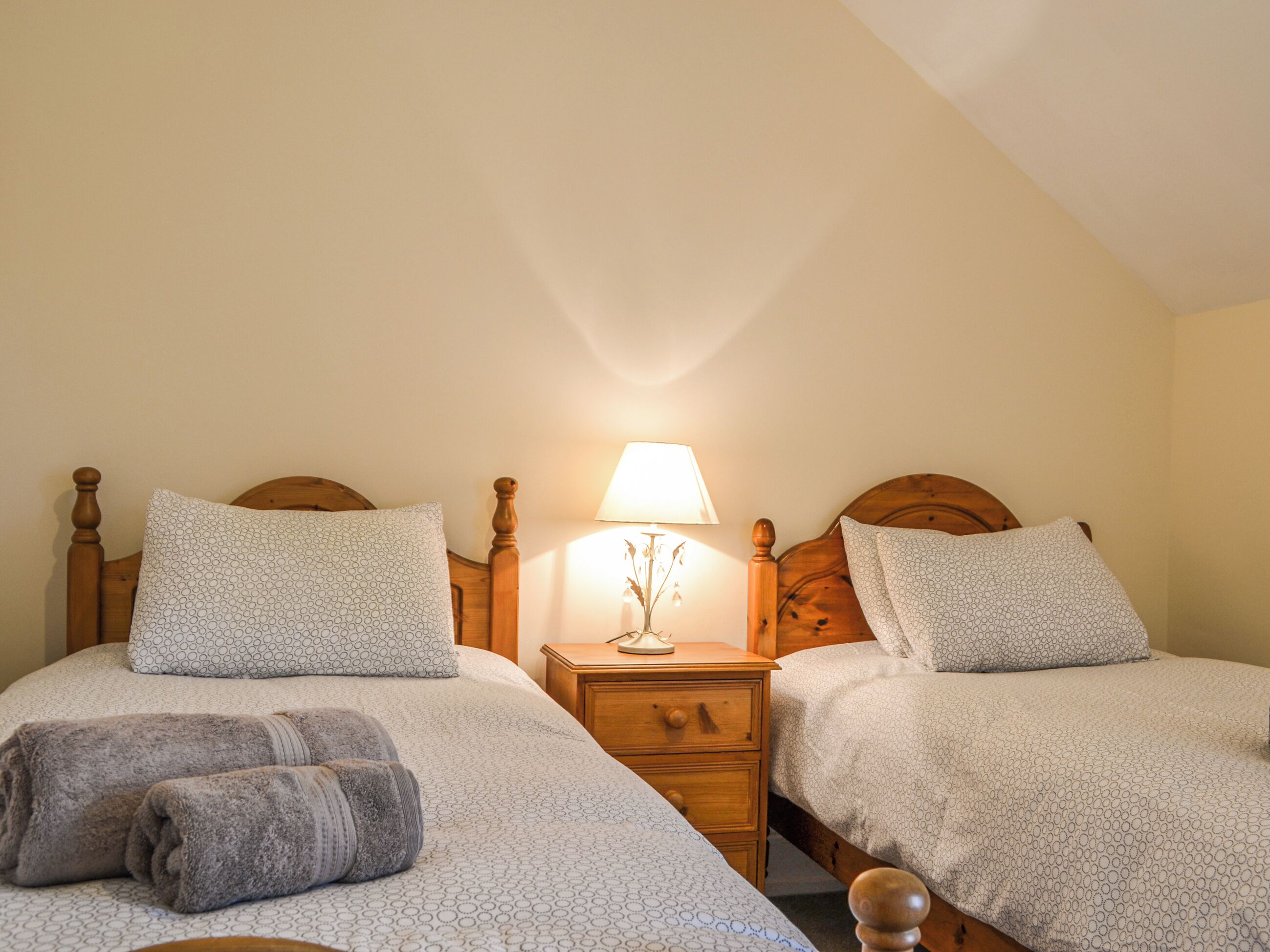 Une chambre avec deux lits, chacun doté d’une tête de lit en bois, d’une table de chevet avec une lampe et d’un luminaire fixé au mur.