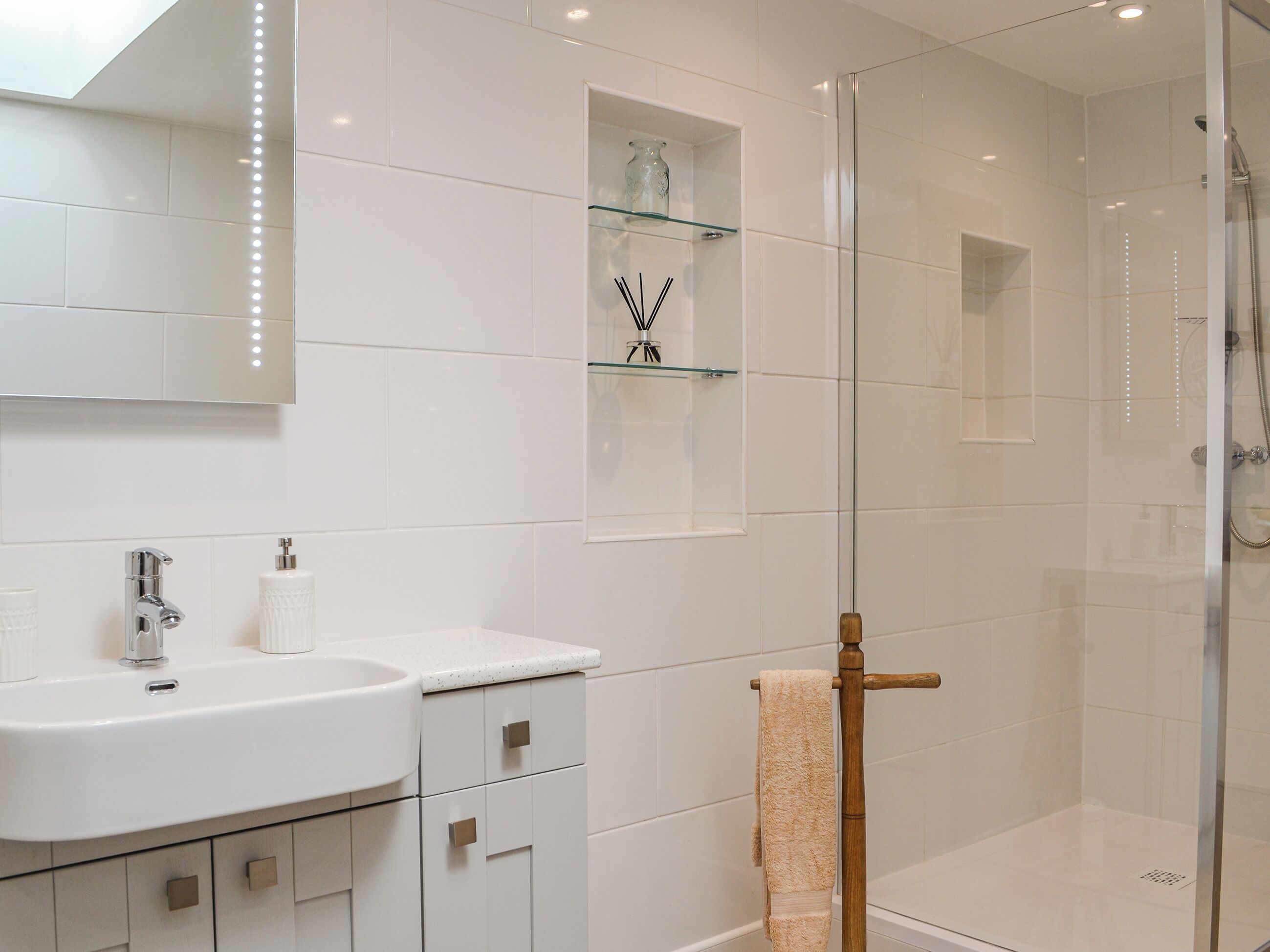 Un baño moderno con cabina de ducha de vidrio, un lavabo blanco con grifo cromado y un estante de vidrio con artículos de aseo.