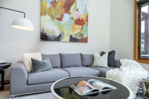 A modern living room with a grey sofa, a round coffee table, and a large abstract painting on the wall. - Mountain Village Bliss! Vistas from Private Hot Tub (Mountain Village)