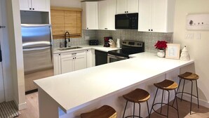 Une cuisine moderne avec des meubles blancs, un réfrigérateur en acier inoxydable, un four à micro-ondes et un grand îlot central doté de tabourets de bar.