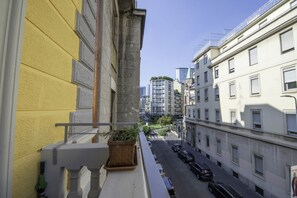 Un balcon agrémenté d’un pot de fleurs, une vue sur une rue de la ville et des immeubles dotés de balcons.