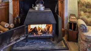 A wood-burning stove with logs, a kettle, and a chair in a cozy room. - Hoopers Farmhouse - UK36307 (Tilshead)