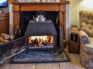 A wood-burning stove with logs, a kettle, and a chair in a cozy room. - Hoopers Farmhouse - UK36307 (Tilshead)