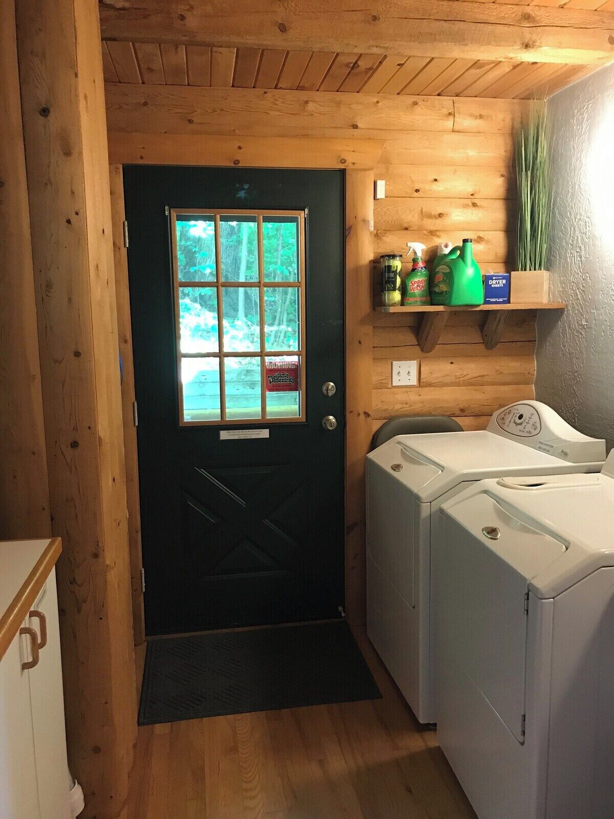 Une buanderie avec une porte en bois, un lave-linge et des produits de nettoyage rangés sur une étagère.