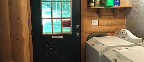 Une buanderie avec une porte en bois, un lave-linge et des produits de nettoyage rangés sur une étagère.