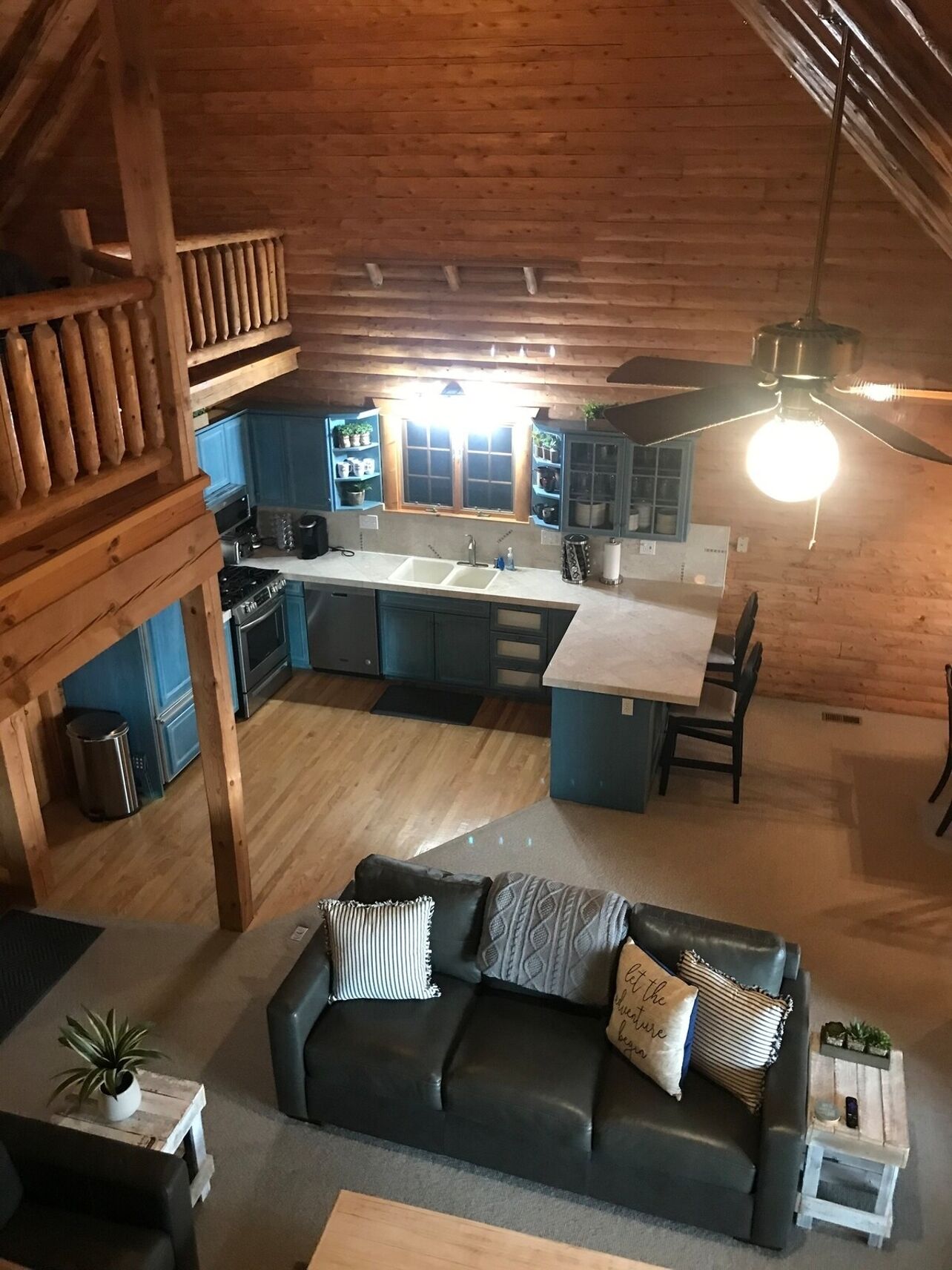 L’intérieur chaleureux d’un chalet avec un plafond en bois, une kitchenette, un coin repas comprenant un canapé et une table basse, et un ventilateur de plafond.
