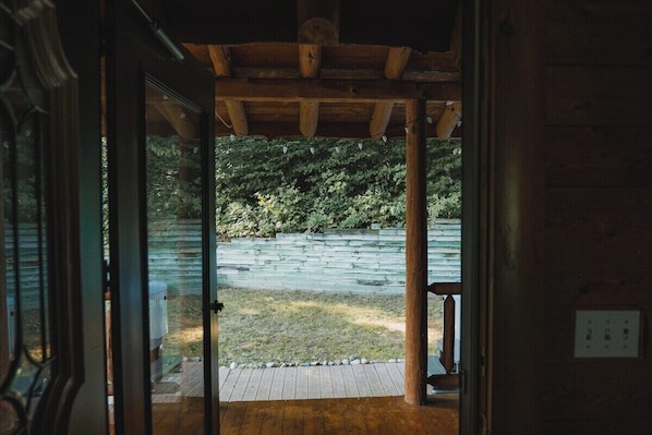 An open wooden door leading to a covered outdoor area with a stone wall and greenery in the background.