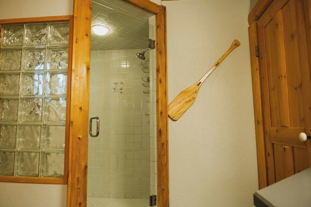 Une salle de bain avec une porte de douche en verre, une porte en bois et un interrupteur mural.