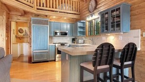 Ein Holzblock-Interieur mit einer Küche, die blauen Schränken, einer zentralen Kochinsel mit Stühlen und einem Essbereich zeigt.