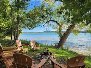 A lakeside seating area with wooden chairs and a fire pit.