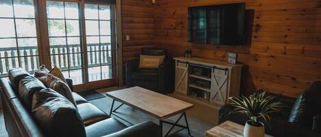 A cozy cabin-style room with a wooden interior, a leather sofa, a coffee table, and a television mounted on the wall.