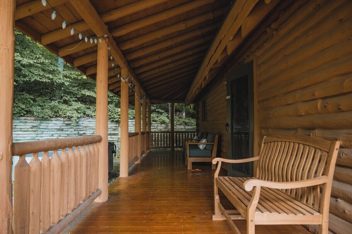 Une cabane en bois avec une véranda, un banc et une vue sur une zone boisée.
