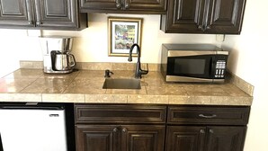 A kitchen with dark wooden cabinets, a stainless steel coffee maker, a black faucet, a black microwave, and a dishwasher.