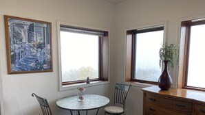 A room with a round table, two chairs, a dresser, and two windows with views of trees.