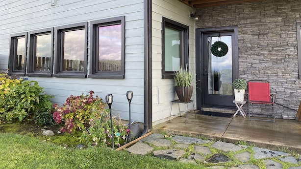 A modern house with a stone facade, a front porch with a red chair, and a wreath on the door.