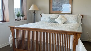 A bedroom with a wooden crib, a large bed with patterned bedding, a floor lamp, and a framed picture on the wall.