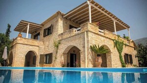 Edificio de piedra con piscina, con ventanas de arco y un porche cubierto.
