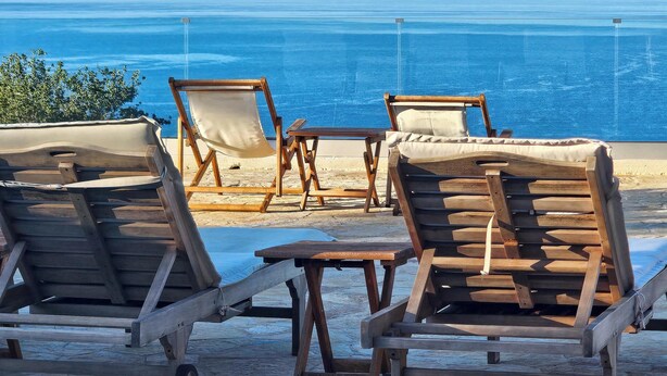 Un área de descanso en la playa con sillones de madera y una mesita, con vista al océano.