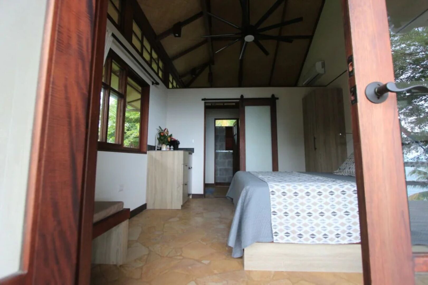 Een slaapkamer met een bed, een klein kitchenette en een stenen vloer.