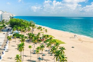 A beach with palm trees, a pool, and a lifeguard tower.