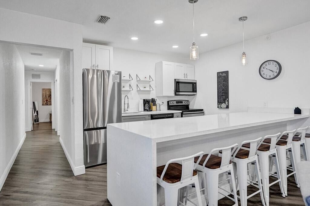 A modern kitchen with white cabinetry, stainless steel appliances, and a bar area with white stools.