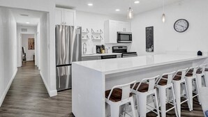 Une cuisine moderne avec des meubles blancs, des appareils en acier inoxydable et un coin bar doté de tabourets blancs.