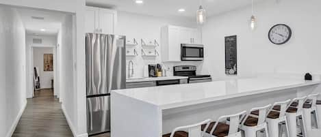 A modern kitchen with white cabinetry, stainless steel appliances, and a bar area with white stools.