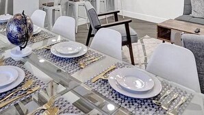 Un coin repas avec une table en verre dressée pour six personnes, entourée de chaises blanches.