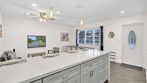 Une cuisine spacieuse dotée d’un grand îlot central, de luminaires suspendus et offrant une vue sur l’extérieur grâce à une fenêtre.