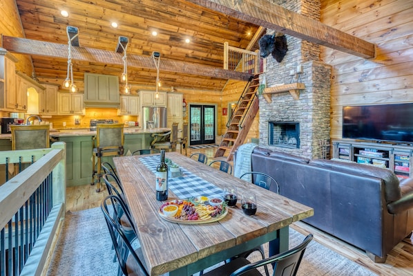A cozy cabin interior with a wooden dining table set for a meal, a stone fireplace, and a comfortable seating area.