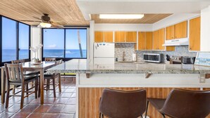 A kitchen with wooden cabinets, a white refrigerator, a microwave, and a sign that reads 'BEACH HOUSE'. - Kuhio Shores, #214. Kauai’s Best Location! Spectacular Oceanfront Condo (Koloa)