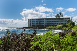 Un hotel de varios pisos con balcones, situado cerca de una costa rocosa y vistas al océano.