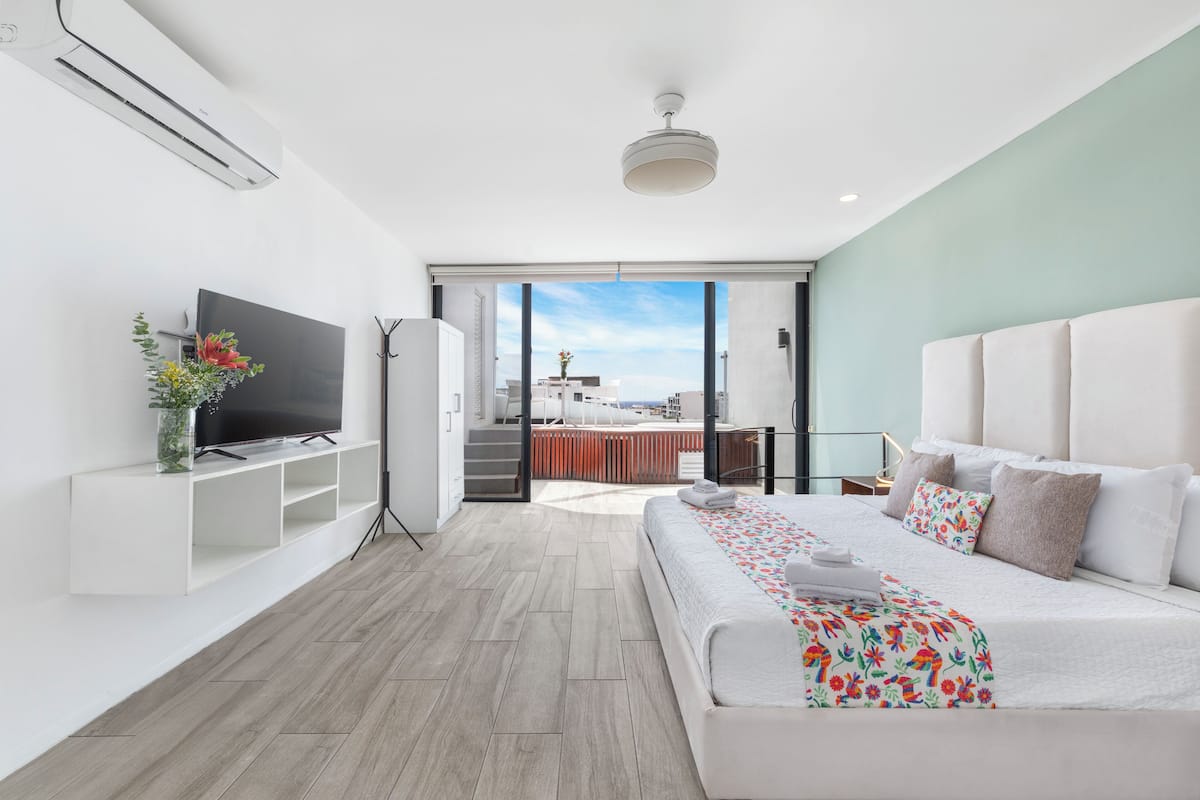 Une chambre d’hôtel moderne dotée d’une télévision à écran plat, d’un canapé-lit, d’une grande fenêtre offrant une vue agréable et d’un ventilateur de plafond.