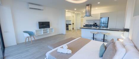 A modern hotel room with a large bed, a TV, a small seating area, and a kitchenette.