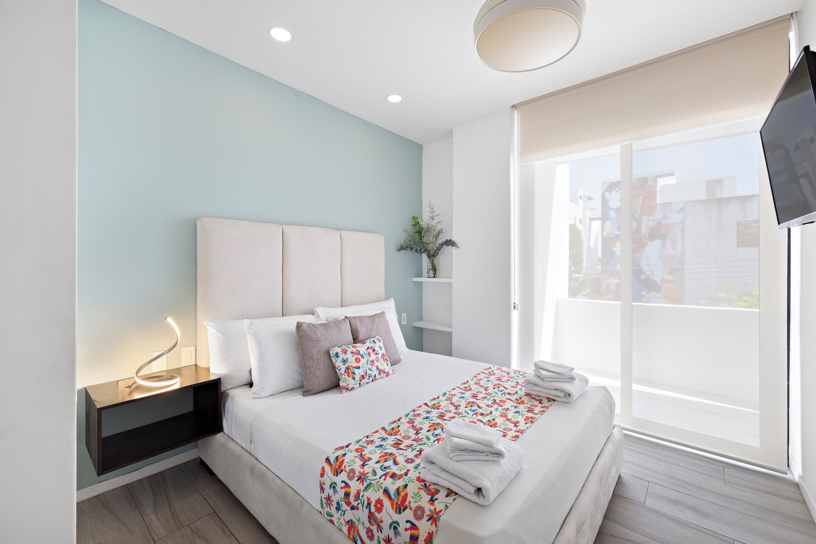Quarto de hotel moderno com cama, mesa de cabeceira, televisão e vista para o exterior.