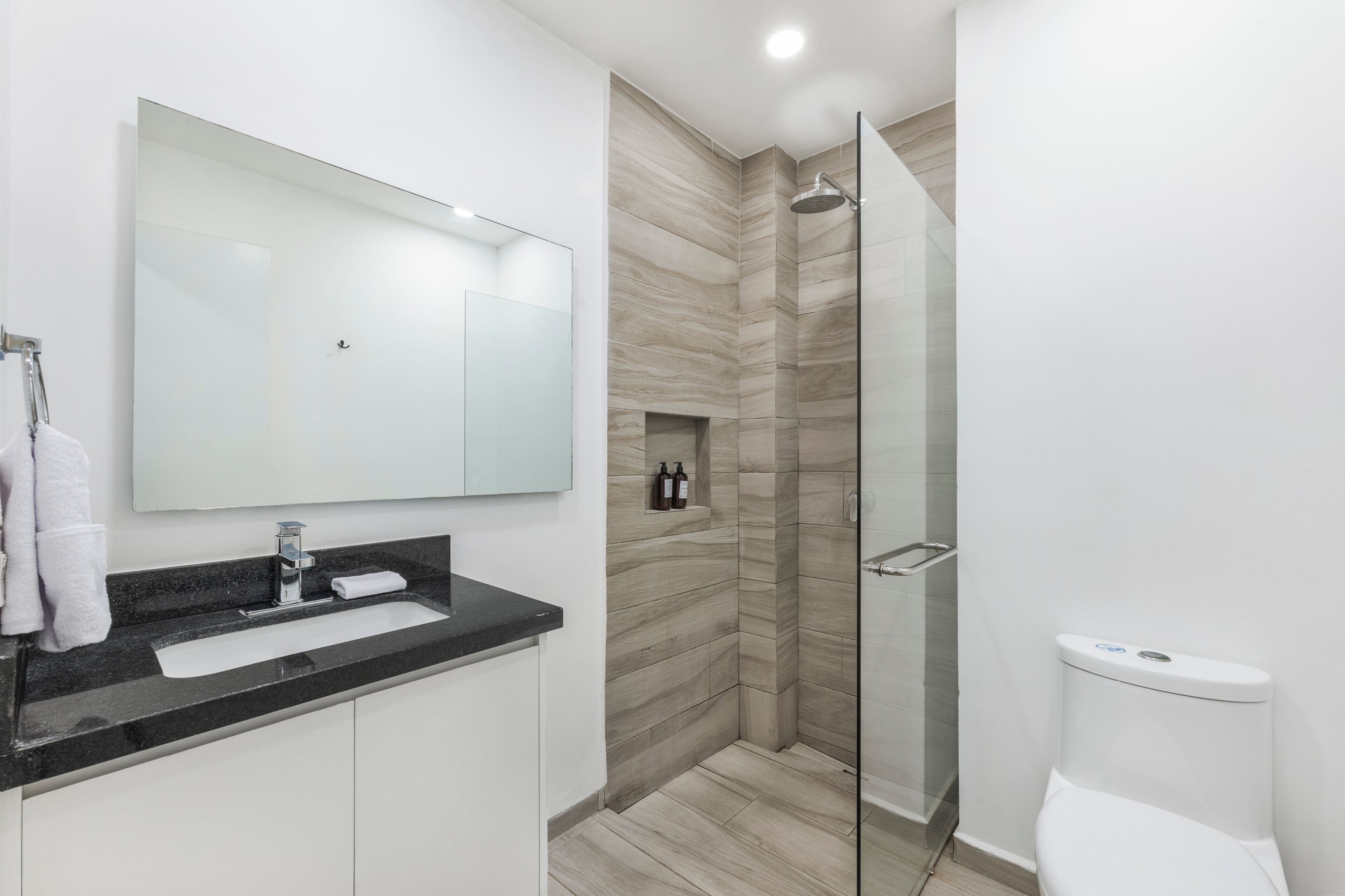 A modern bathroom with a large mirror, a sink, a shower, and a toilet.